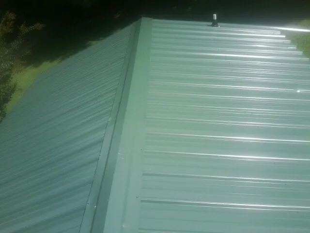 New green metal panels meeting at the ridge of a roof — Flat Roof Repair work by our crew in Ontario